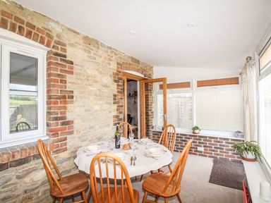 A dining area with a round table set for four and wooden chairs in a room with brick and stone walls at Knapp Cottage in Chickerell