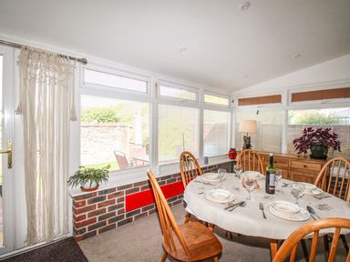 A dining room with a round table set for five people wooden chairs and windows with blinds at Knapp Cottage in Chickerell