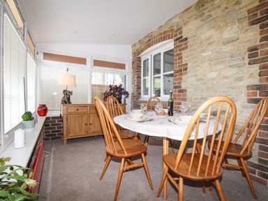 A dining area with a round table set for four and wooden chairs next to a stone wall at Knapp Cottage in Chickerell