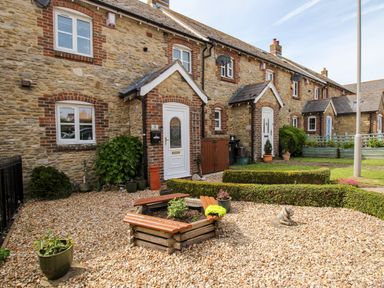 A stone cottage with white doors surrounded by a gravel garden and wooden planter at Knapp Cottage in Chickerell