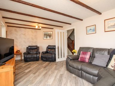 A living room with leather sofas a wooden TV stand a flat screen TV and pictures on the walls at Knapp Cottage in Chickerell