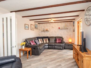 A living room with a leather corner sofa cushions wooden side table wall shelves wall clock and wooden TV stand at Knapp Cottage in Chickerell