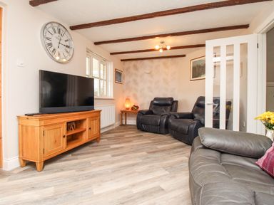 A living room with leather chairs a wooden TV stand with a television and a large clock on the wall at Knapp Cottage in Chickerell