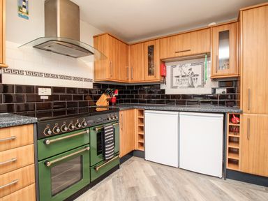 A kitchen with wooden cabinets a green oven black and white tiled backsplash and two white appliances under the counter at Knapp Cottage in Chickerell