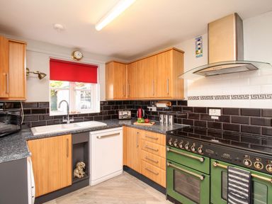 A kitchen with wooden cabinets a green oven black tiled backsplash and a window with a red blind at Knapp Cottage in Chickerell
