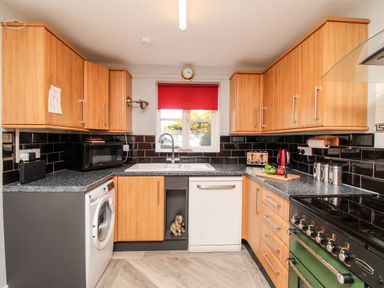 A kitchen with wood cabinets black tile backsplash and appliances at Knapp Cottage in Chickerell