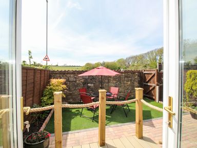 A small fenced garden with artificial grass a round table four red chairs and a red umbrella at Knapp Cottage in Chickerell