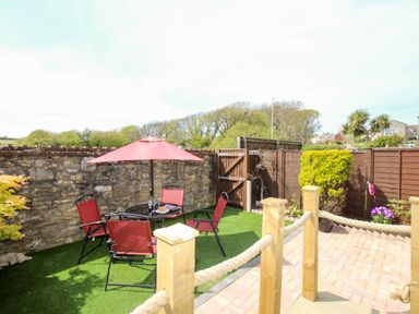 A small garden with red patio chairs and table with umbrella on artificial grass at Knapp Cottage in Chickerell