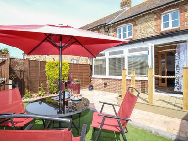 A brick house with a patio table and red chairs under a red umbrella in the garden at Knapp Cottage in Chickerell