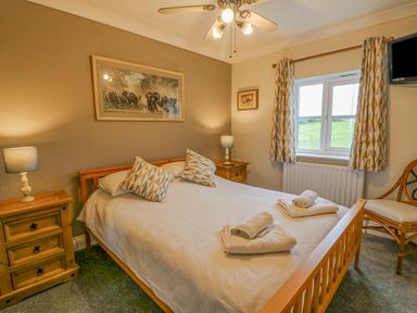 A bedroom with a double bed two bedside tables with lamps a chair and a window at Knapp Cottage in Chickerell