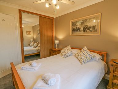 A bedroom with a double bed with patterned pillows bedside tables lamps and a wardrobe with sliding doors at Knapp Cottage in Chickerell
