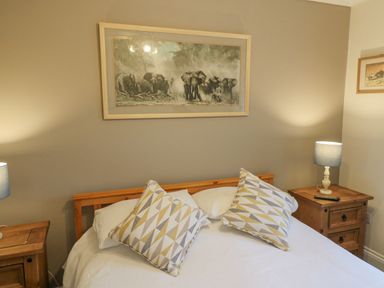 A bedroom with a wooden bed frame two patterned pillows two wooden bedside tables with lamps and elephant pictures on the wall at Knapp Cottage in Chickerell