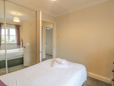 A bedroom with a bed a folded towel on the bed mirrored wardrobe and a window at Knapp Cottage in Chickerell