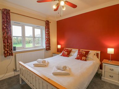 A bedroom with a double bed two pillows with animal prints bedside tables lamps a window with curtains and a ceiling fan at Knapp Cottage in Chickerell