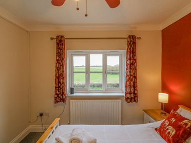 A bedroom with a window showing a green field outside and a bed with white sheets and red elephant pillow at Knapp Cottage in Chickerell
