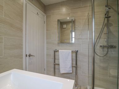 A bathroom with a white door a mirror a towel rack with a towel a showerhead and a white sink at Knapp Cottage in Chickerell