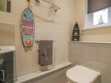 A bathroom with a toilet a gray towel hanging on a rail a decorative surfboard and boat-shaped shelf by a window at Knapp Cottage in Chickerell