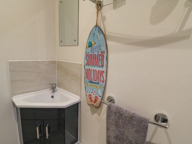 A small corner sink with cabinet below a wall mirror and a towel rack with a gray towel in a bathroom at Knapp Cottage in Chickerell