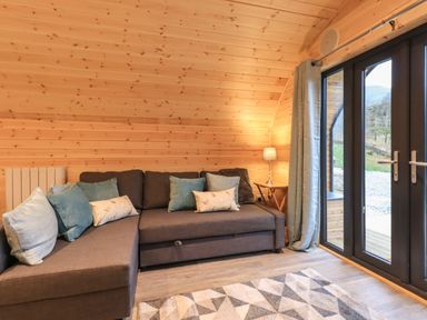A living room with a gray sofa with cushions a side table with a lamp and glass doors at Jenny - Crossgate Luxury Glamping in Hartsop near Glenridding