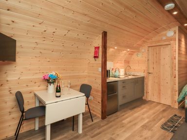 A wooden interior with a small dining table with two chairs and a kitchenette with grey cabinets and a sink at Jenny - Crossgate Luxury Glamping in Hartsop near Glenridding
