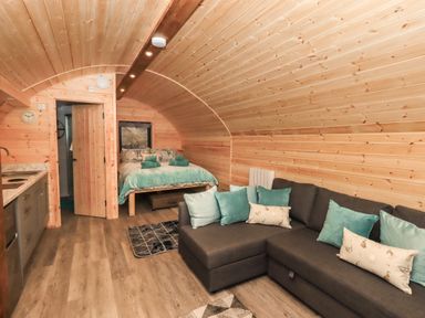 A wooden interior room with a bed, a couch with cushions, and a kitchen area at Jenny - Crossgate Luxury Glamping in Hartsop near Glenridding