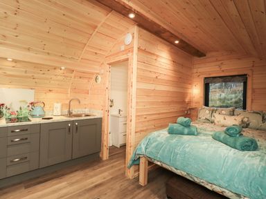 A wooden cabin interior with a kitchenette and a bed with blue bedding at Jenny - Crossgate Luxury Glamping in Hartsop near Glenridding