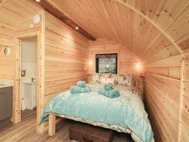 A bedroom with a double bed with blue bedding and towels inside a wooden cabin at Jenny - Crossgate Luxury Glamping in Hartsop near Glenridding