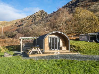 A wooden glamping pod with a picnic table and a hot tub on a deck surrounded by grass and hills at Jenny - Crossgate Luxury Glamping in Hartsop near Glenridding