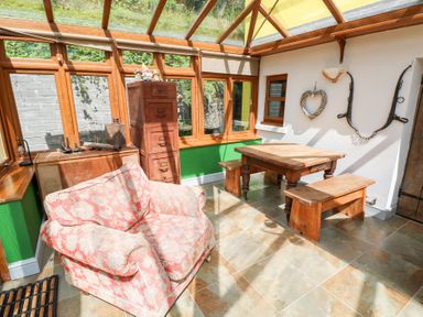 A conservatory with wooden furniture and large windows at The Woodlands Lower Level Stepaside