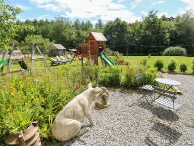 A garden with a swing set, playhouse, and seating area at The Woodlands Lower Level in Stepaside