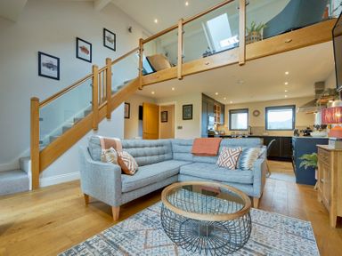 An open-plan living room and kitchen with a grey sectional sofa and glass coffee table at Riverside Park 6 in Keswick
