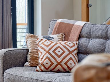 A gray fabric sofa with patterned cushions and a blanket near a window at Riverside Park 6 in Keswick