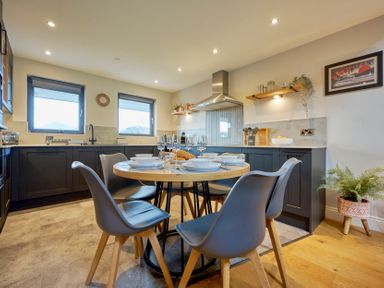 A kitchen with a round dining table set with plates glasses and croissants at Riverside Park 6 in Keswick