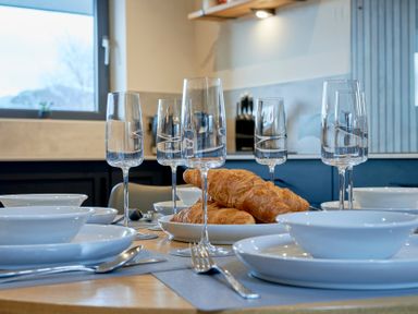 A dining table set with croissants on a plate champagne glasses and white plates at Riverside Park 6 in Keswick