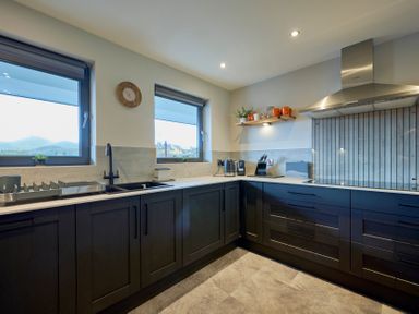 A kitchen with dark cabinets black sink windows and stainless steel extractor fan at Riverside Park 6 in Keswick
