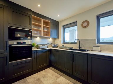 A kitchen with dark cabinets a countertop with a sink oven toaster and glass shelves at Riverside Park 6 in Keswick