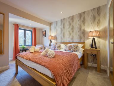 A bedroom with a wooden bed with orange bedding two bedside tables with lamps and a window with orange curtains at Riverside Park 6 in Keswick