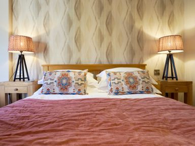 A bed with patterned cushions and a pink blanket with bedside tables and lamps at Riverside Park 6 in Keswick