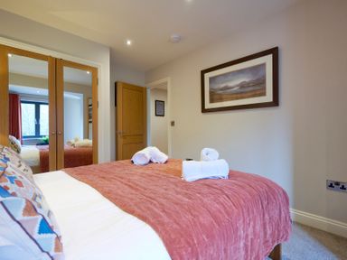 A bedroom with a bed covered with a rust-coloured blanket and pillows a wooden wardrobe with mirrored doors and a framed landscape picture on the wall at Riverside Park 6 in Keswick