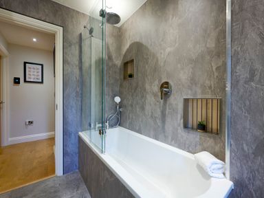 A bathroom with a bathtub shower combination and gray tiled walls at Riverside Park 6 in Keswick