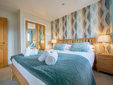 A bedroom with a wooden bed frame and bedside tables with lamps at Riverside Park 6 in Keswick
