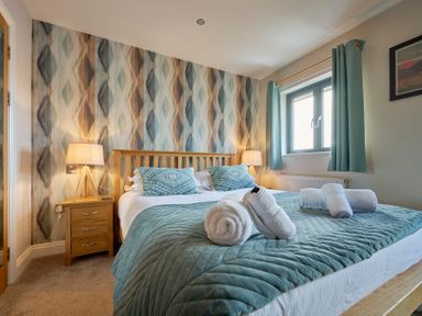 A bedroom with a double bed bedside tables lamps window with curtains and patterned wallpaper at Riverside Park 6 in Keswick