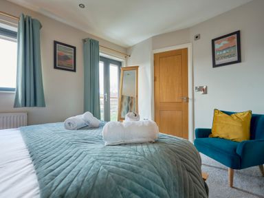 A bedroom with a bed covered by a quilt and towels on top a blue armchair with a yellow cushion a wooden door and two framed pictures on the walls at Riverside Park 6 in Keswick