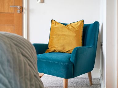 A blue armchair with a yellow cushion on a carpeted floor beside a wooden door at Riverside Park 6 Keswick