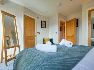 A bedroom with a bed covered in a quilted blanket and rolled towels with wooden doors and a full-length mirror at Riverside Park 6 in Keswick