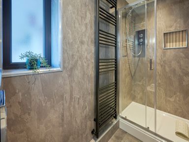 A bathroom with a walk-in shower a black towel radiator and a window with a plant at Riverside Park 6 in Keswick
