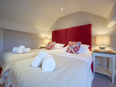 A bedroom with two single beds with red headboards rolled towels and bedside tables with lamps at Riverside Park 6 in Keswick