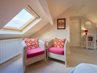 Two wicker armchairs with red cushions in a room with a skylight window radiator a small side table with a lamp a wall painting a door a bookshelf and a mirror at Riverside Park 6 in Keswick