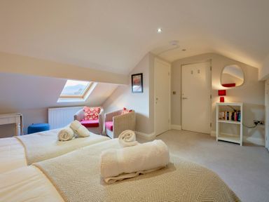 A bedroom with two beds with towels on them two armchairs under a skylight window a small white bookshelf with books and a lamp Riverside Park 6 Keswick