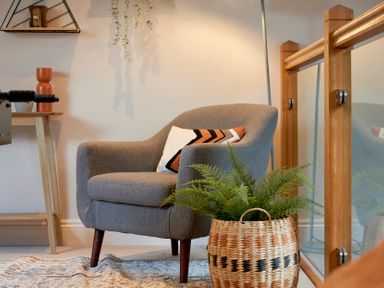 A grey armchair with a patterned cushion next to a woven basket with green plants in a room at Riverside Park 6 in Keswick